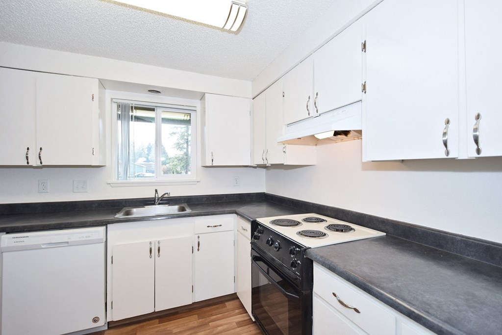 The Firs:  a kitchen with white cabinets and black countertops