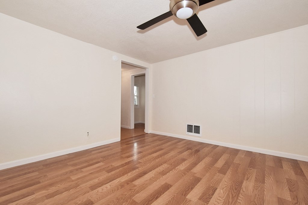 an empty living room with wood floors and a ceiling fan