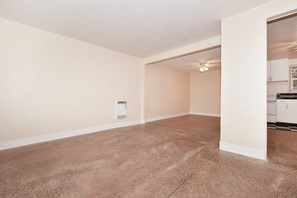 the spacious living room and kitchen of an empty home with carpeting and white walls