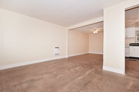 the spacious living room and kitchen of an empty home with carpeting and white walls