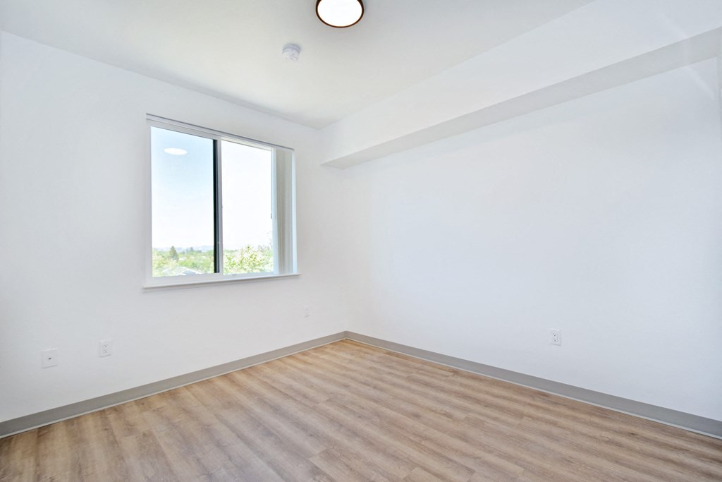 an empty bedroom with a window and hardwood floors