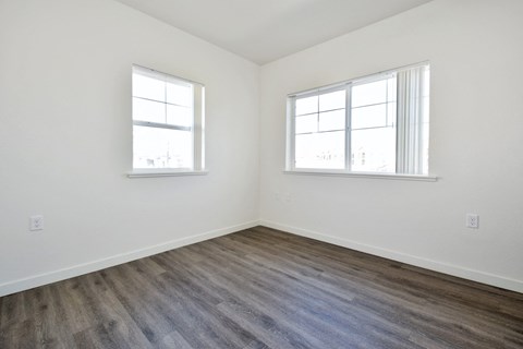 a bedroom with white walls and wood flooring and two windows