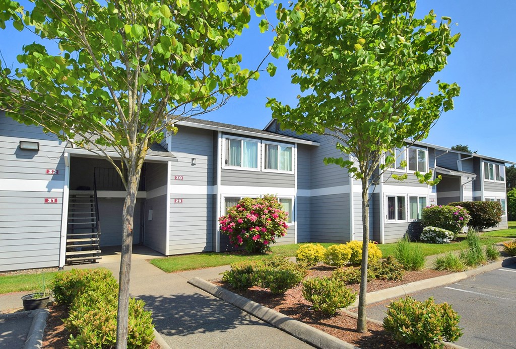 a gray building with white trim and a tree in front of it