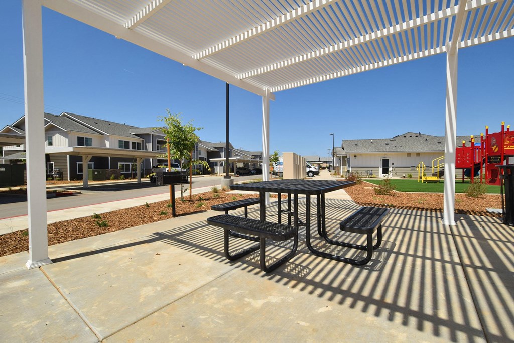 a picnic table and benches under a pergola at the whispering winds apartments in pearland