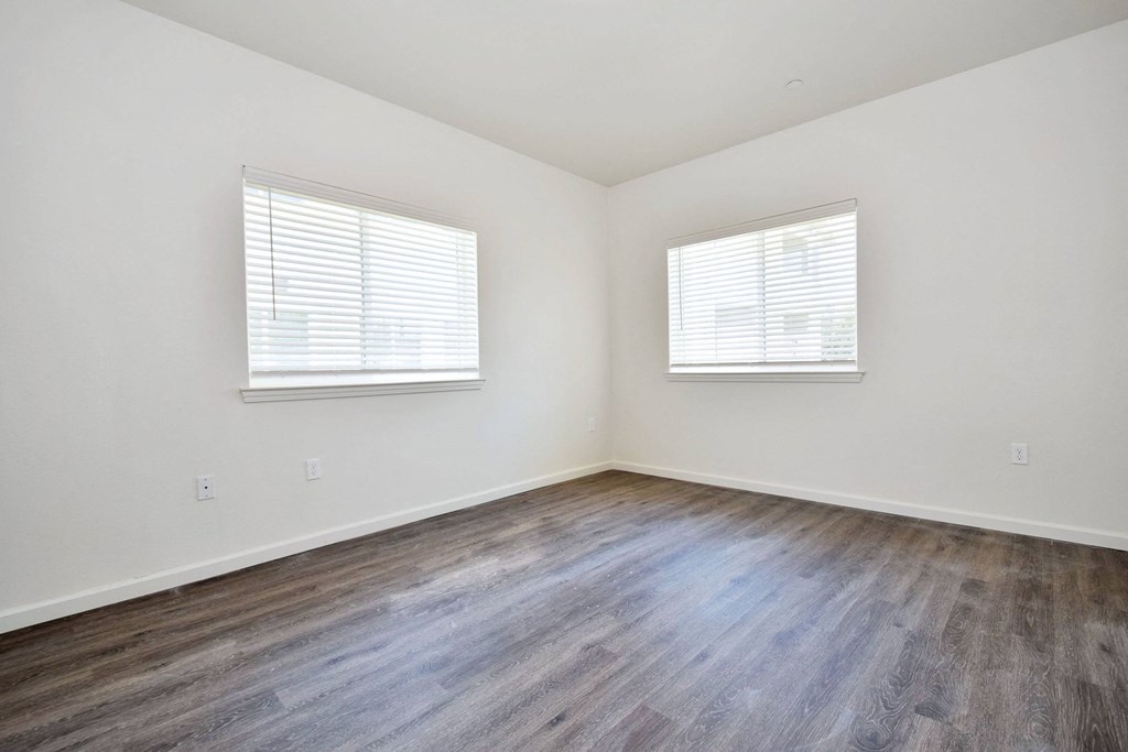 a bedroom with hardwood floors and two windows