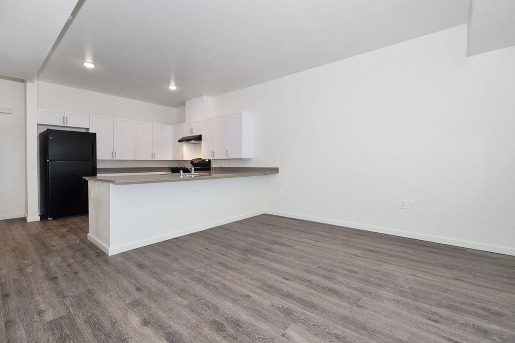 an empty living room with a kitchen in the background