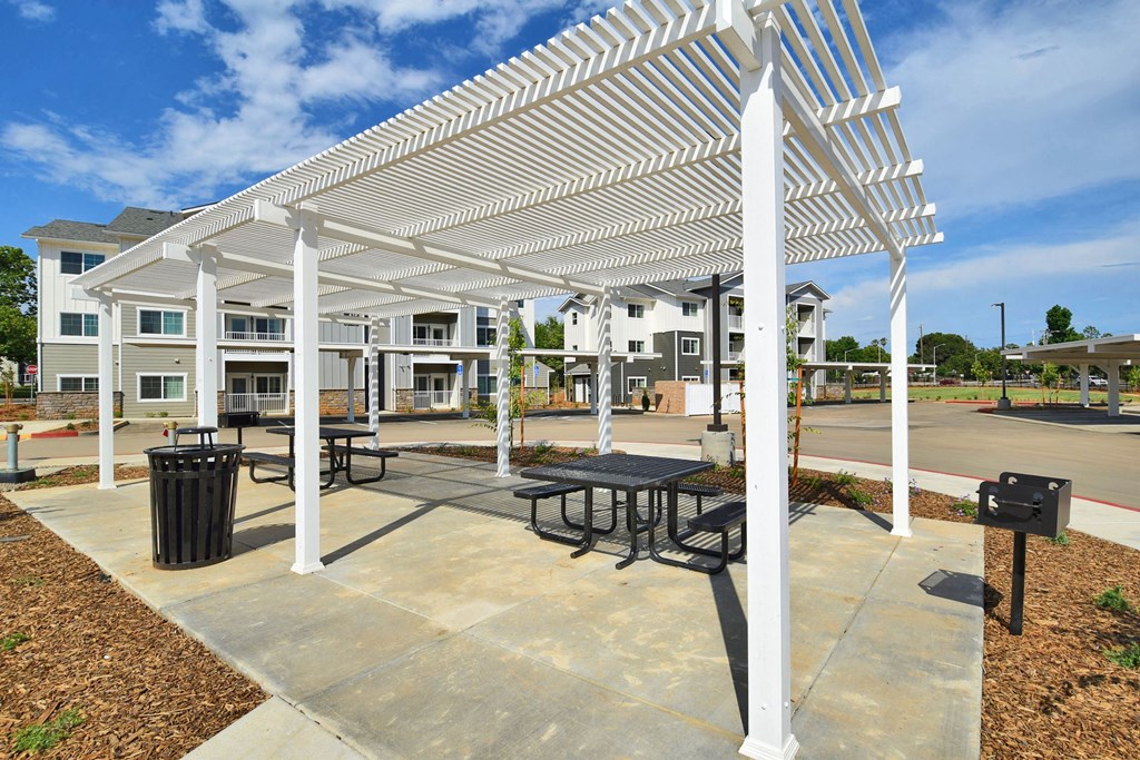 a picnic area with tables and benches under a white awning with apartment buildings in the