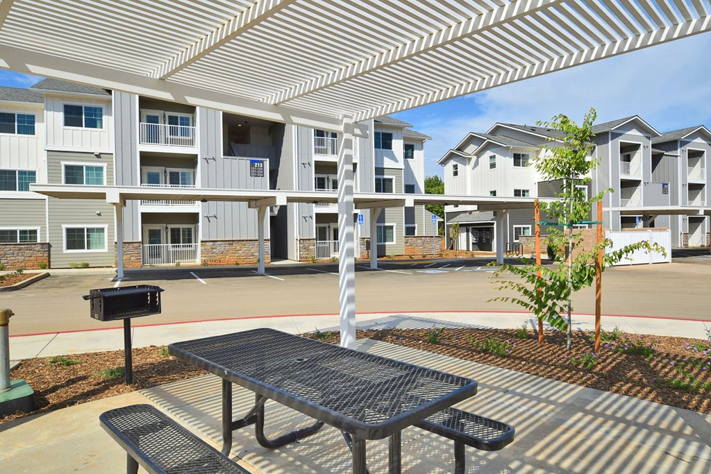 a picnic table and grill sit under a white awning in front of an apartment complex