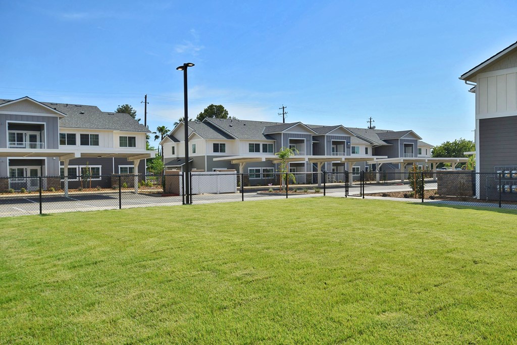 a large grassy area with a fenced in yard in front of a row of houses