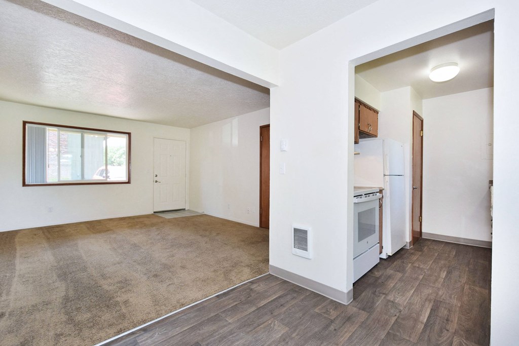 an empty living room with a kitchen in the background