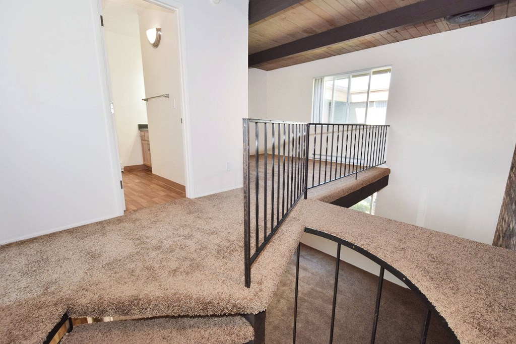 a view from the top of a staircase in a home with white walls and a wooden ceiling