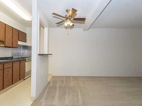 an empty living room with a ceiling fan and a kitchen
