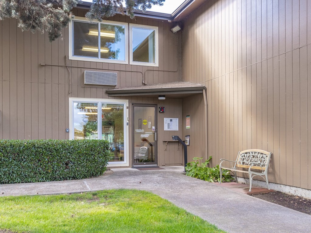 the front door of a home with a bench and a lawn