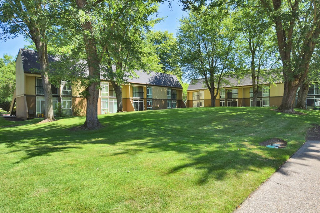 a grassy area with trees in front of an apartment building