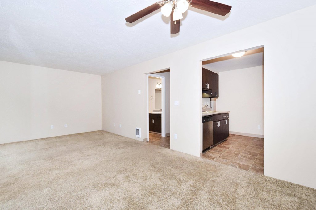 a living room with a ceiling fan and a kitchen in the background