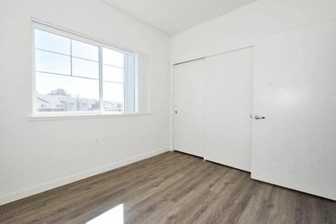 a bedroom with white walls and a window and wood floors