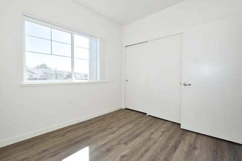 a bedroom with white walls and wood flooring and a window