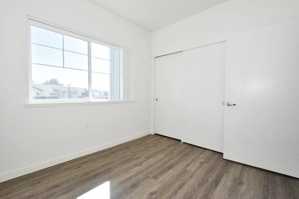 a bedroom with white walls and wood flooring and a window