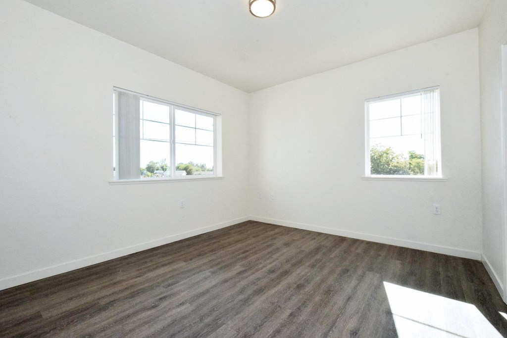 an empty room with white walls and wood floors and two windows