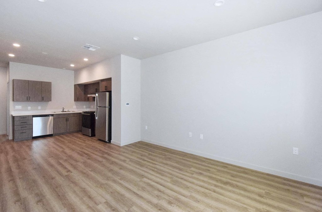 an empty living room with a kitchen in the background