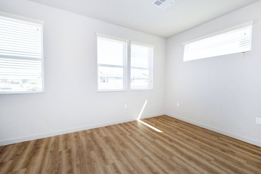 an empty room with a hardwood floor and three windows