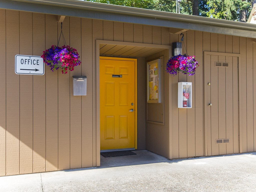 the front of a building with a yellow door and two hanging flowers