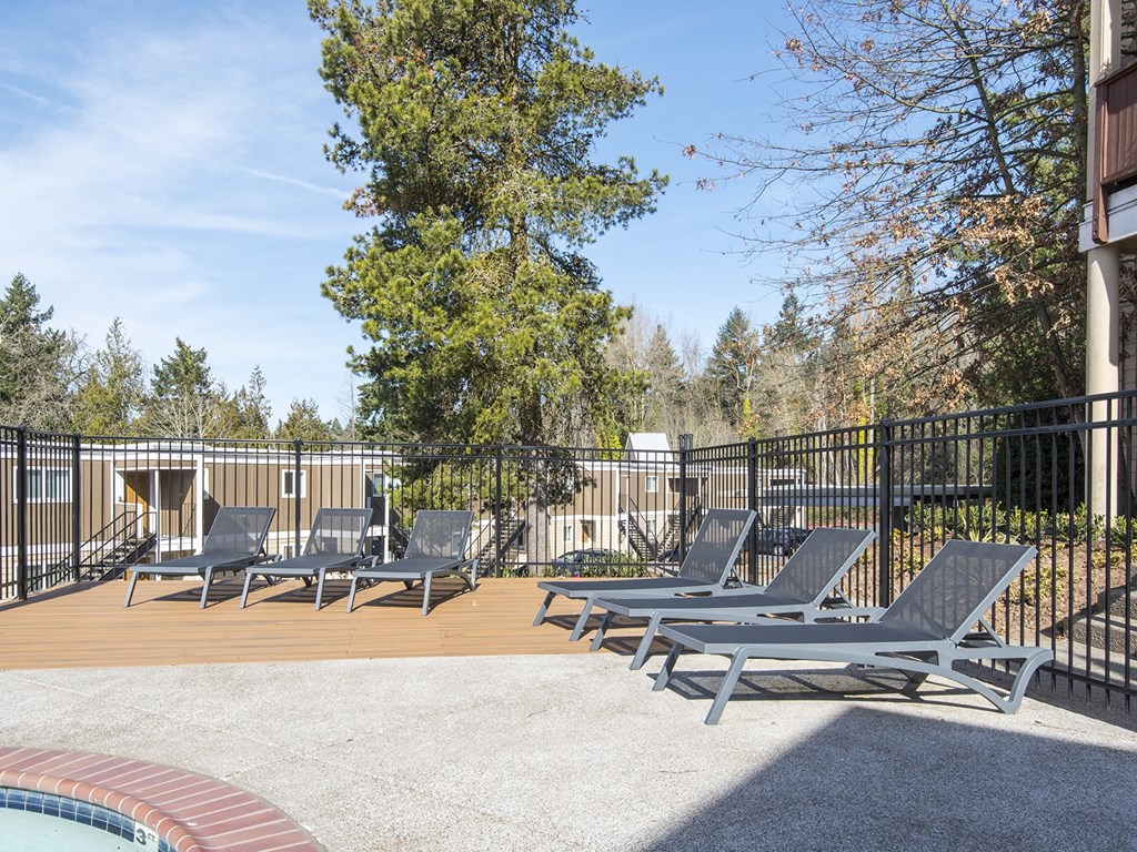 a patio with lounge chairs and a pool with trees in the background