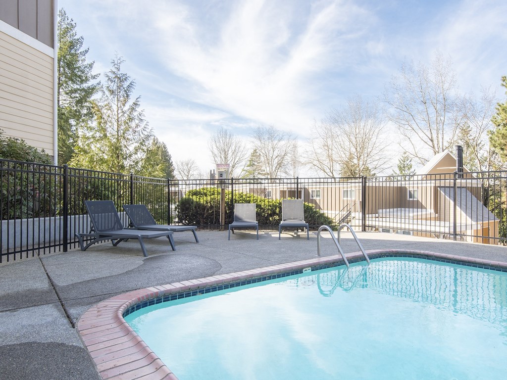 our resort style swimming pool is next to our building with chairs and a fence