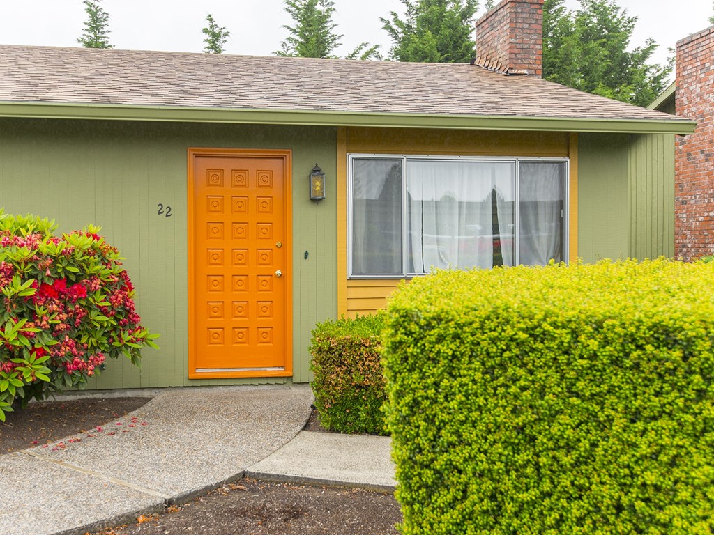 the front of a green house with an orange door