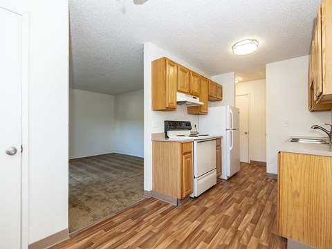 an open kitchen and living room with wood flooring and white appliances
