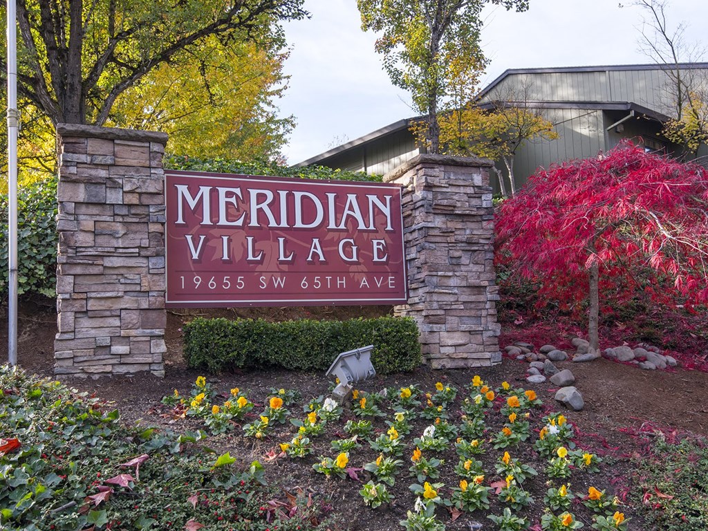a sign that says meridian village with a red tree in the background