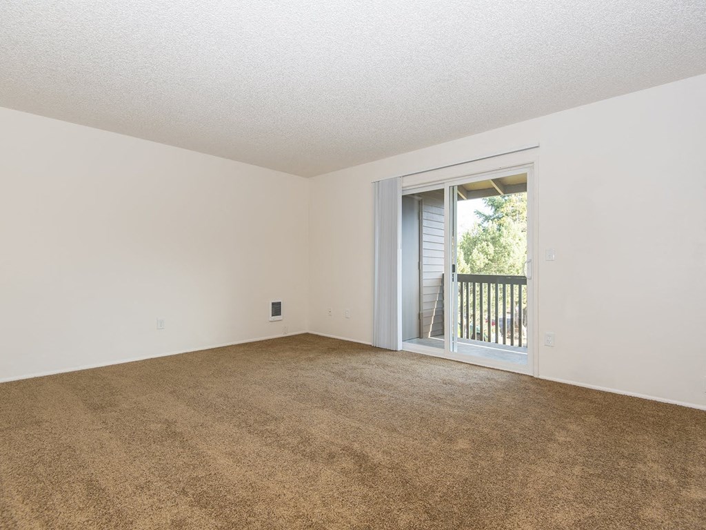 an empty living room with a sliding glass door to a balcony