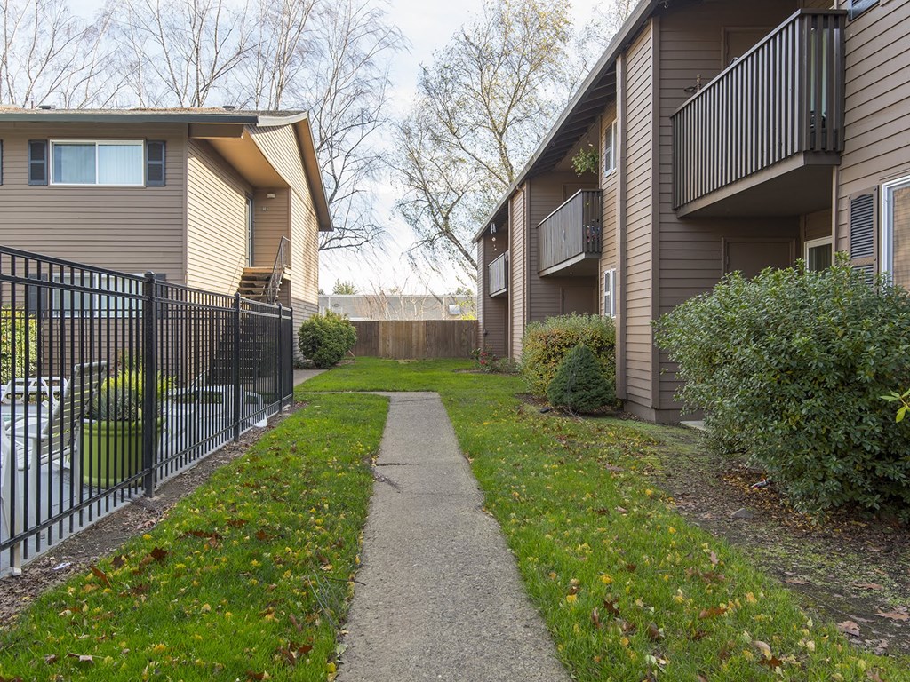 a walkway between two apartment buildings with a yard and a fence