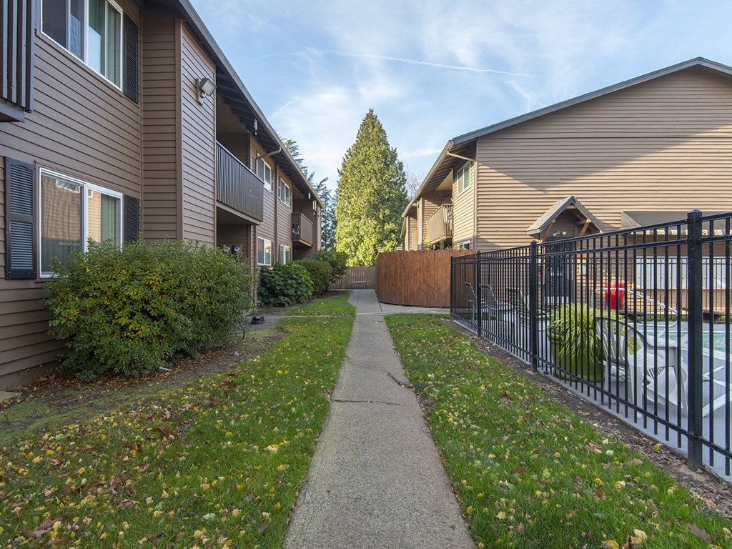 a walkway between two houses with a fence and a pond