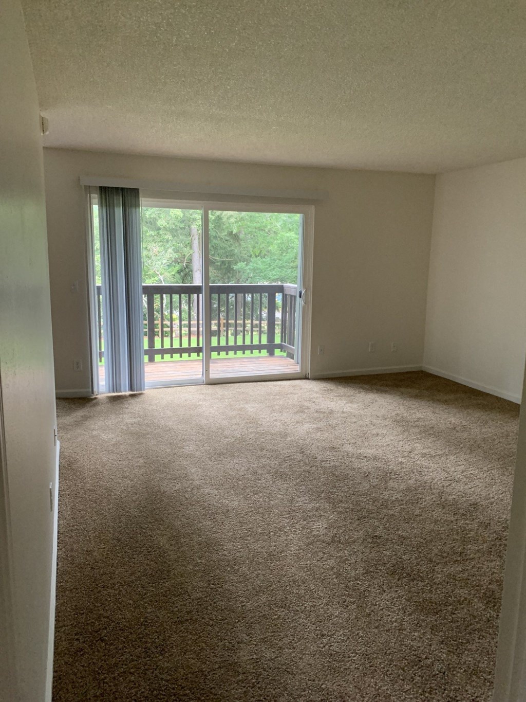 A room with a carpeted floor and a sliding glass door leading to a deck.