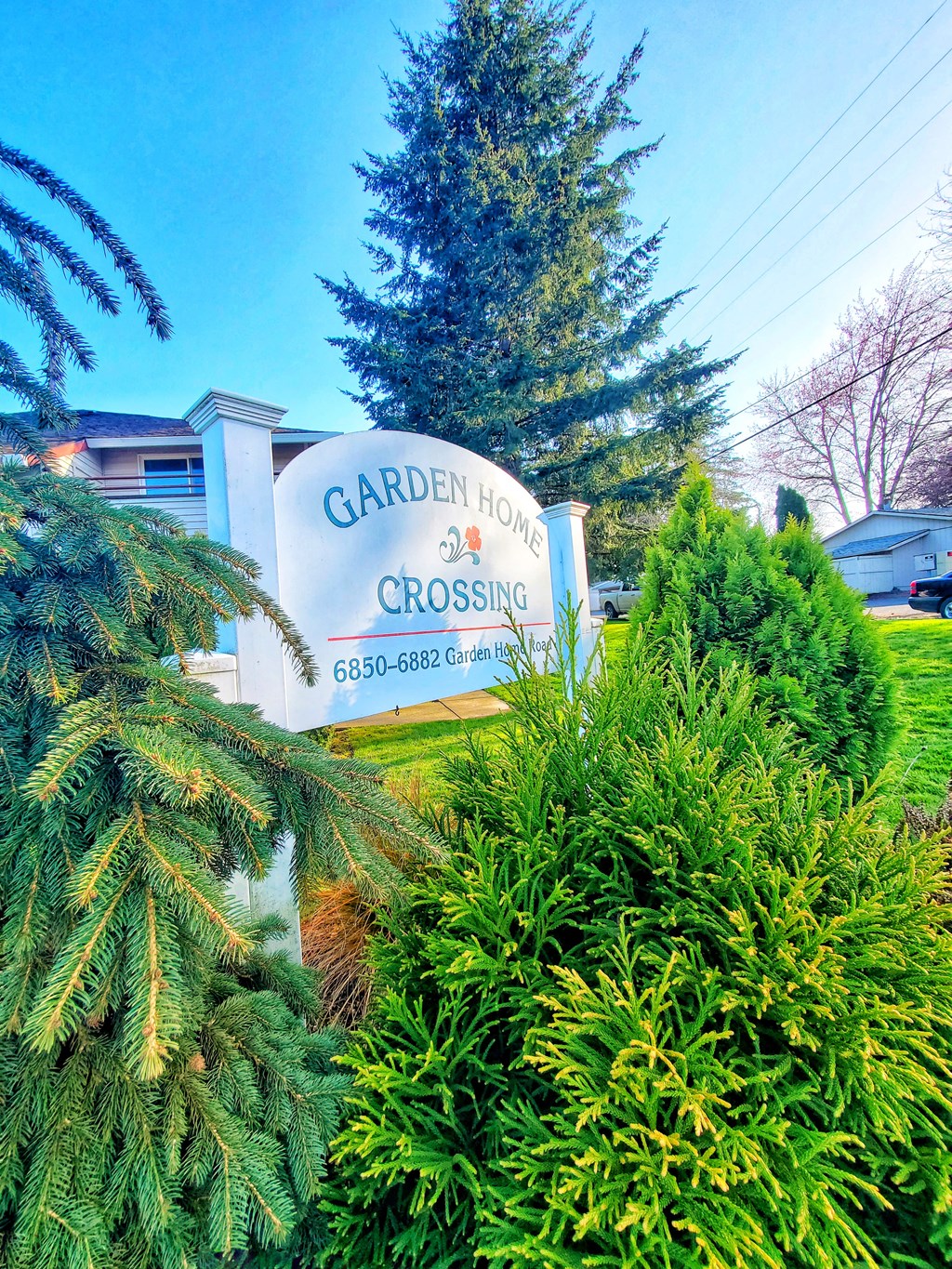 a sign for garden home crossing in front of trees and bushes