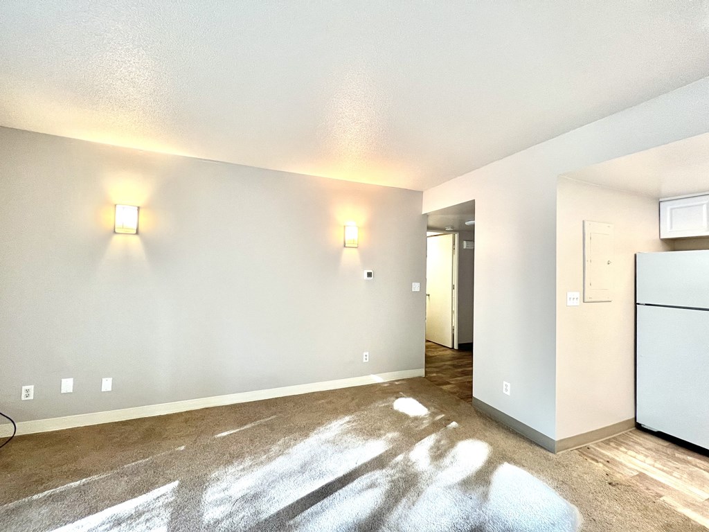 the living room and kitchen of an apartment with white walls and wood floors
