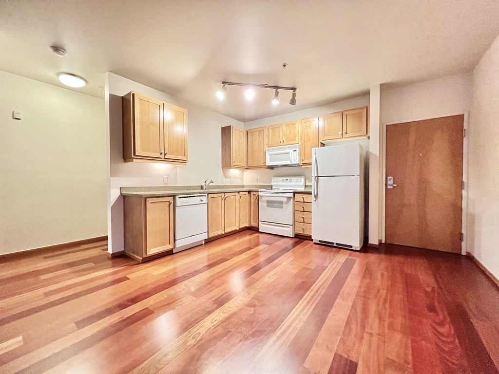 an empty kitchen with wood floors and white appliances