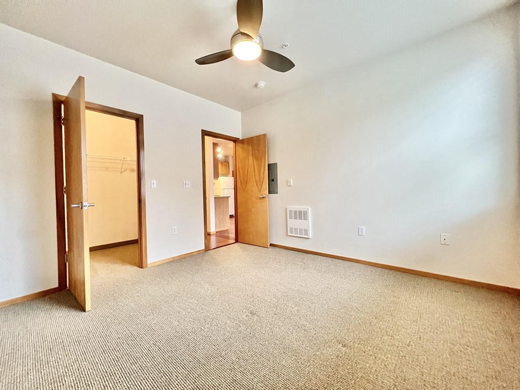 an empty living room with a ceiling fan and a door to a bathroom