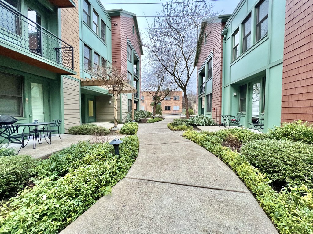a walkway between two apartment buildings with a sidewalk and bushes