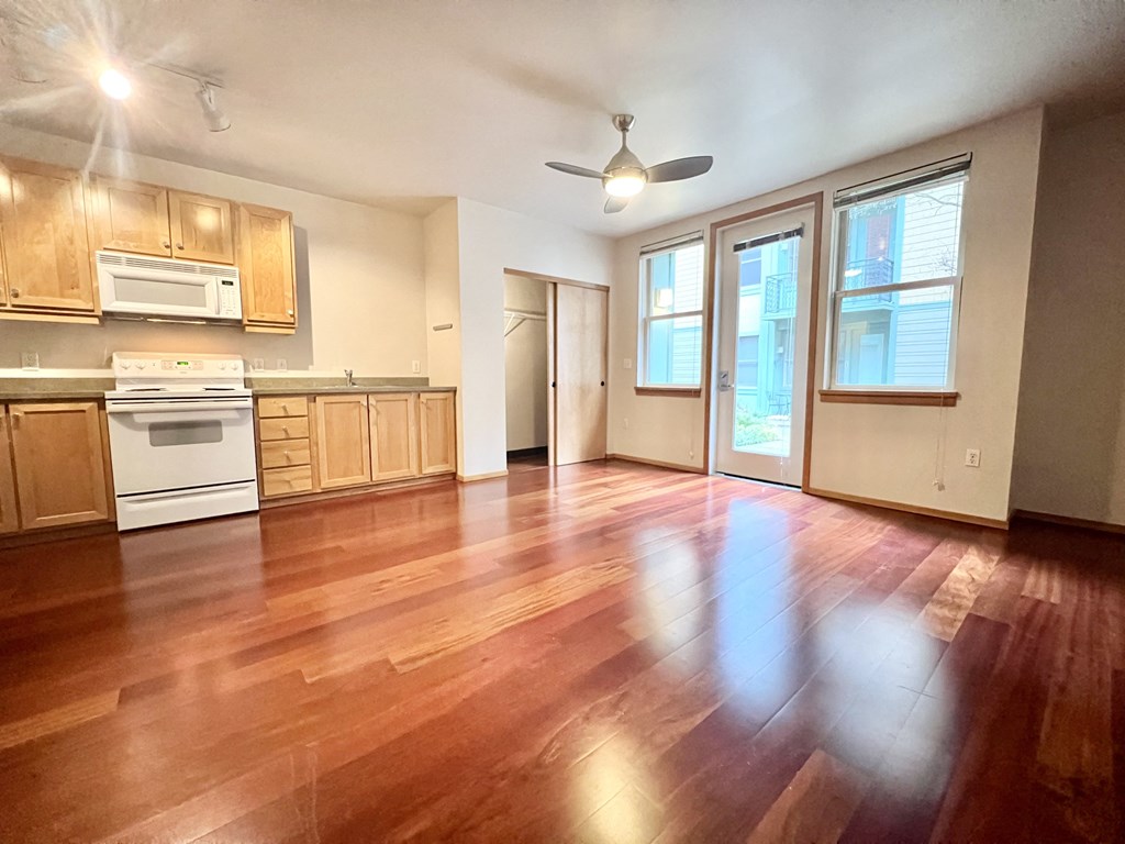 an empty living room and kitchen with wood floors and a ceiling fan