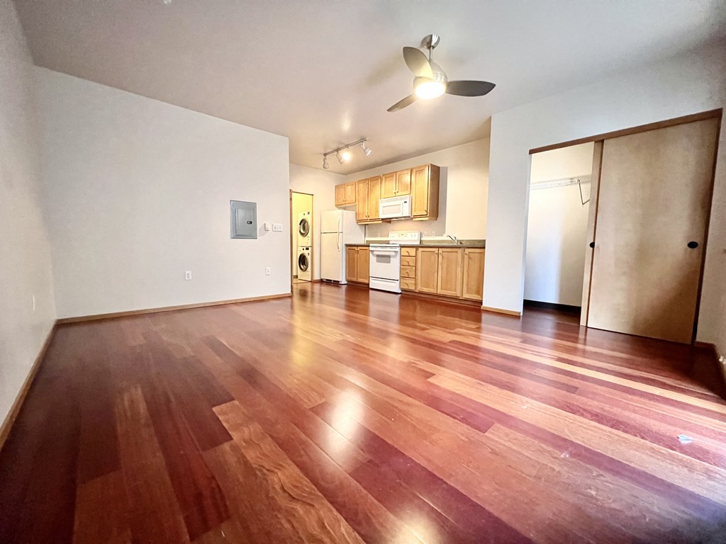 an empty living room with wood floors and a kitchen