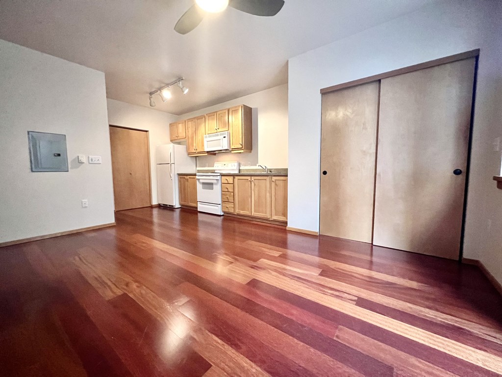 an empty living room with wood floors and a kitchen