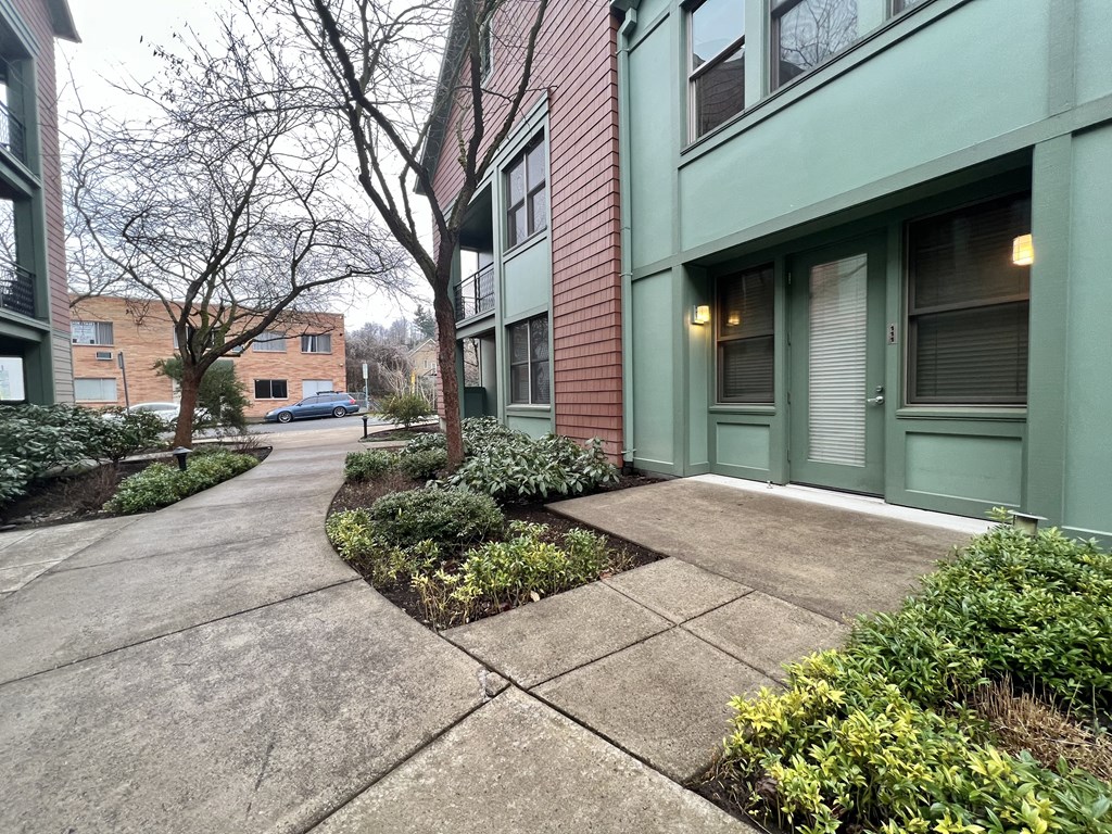 a sidewalk in front of a green and brick apartment building