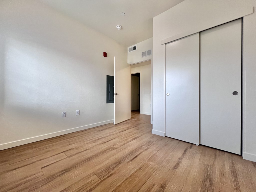 A room with white walls and wooden flooring, featuring a white door and a black door.