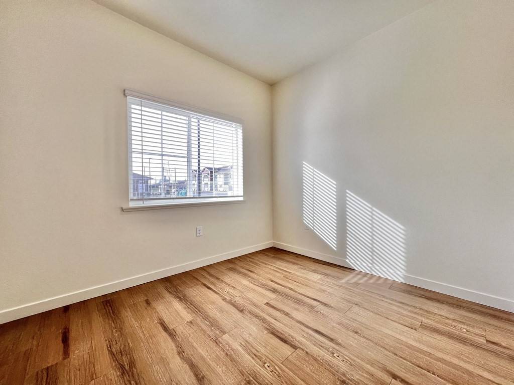 A room with wooden flooring and a window with blinds.