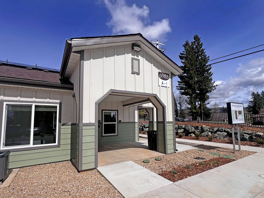 A small white building with a green trim and a sign that reads "6985 A11" is shown.