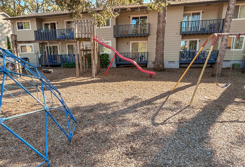 A playground with a blue swing set and a red slide in front of apartment buildings.