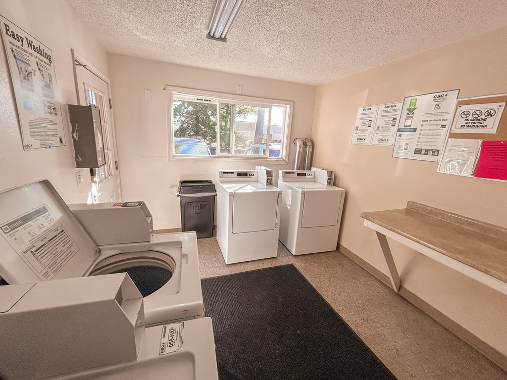 A laundry room with a washer and dryer, a trash can, and a bench.