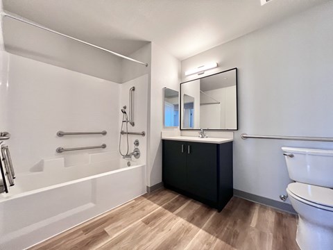 A modern bathroom with a white tub, black vanity, and wooden flooring.